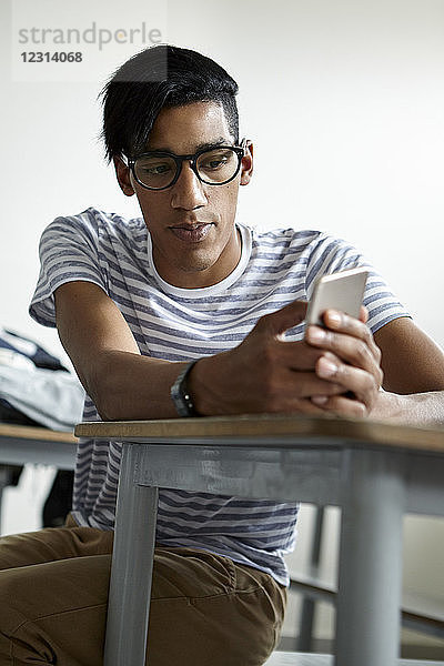 Student am Schreibtisch sitzend mit Smartphone