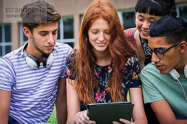 Gruppe von College-Studenten  die gemeinsam im Freien ein digitales Tablet betrachten