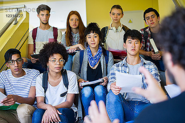 Eine Gruppe von Studenten sitzt auf einer Treppe und hört einer informellen Präsentation zu