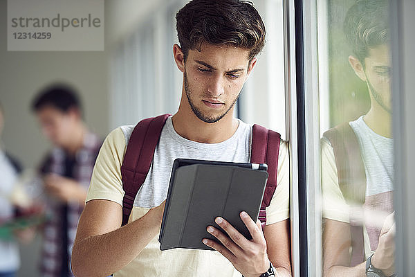 Männlicher Student  der ein digitales Tablet im Korridor benutzt