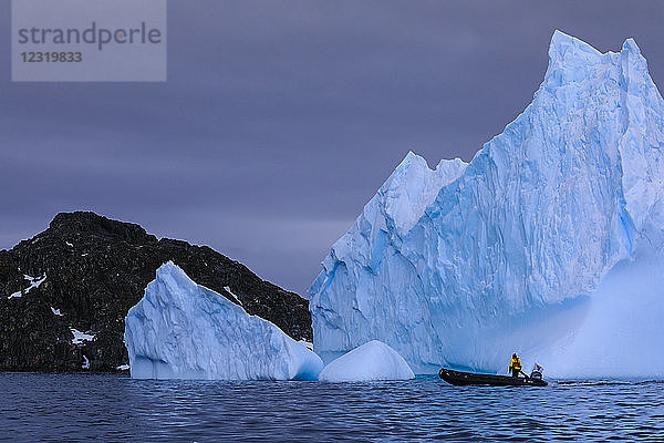 Person im Zodiac schaut auf einen riesigen blauen Eisberg  in der Nähe von Torgersen Island  Anvers Island  Antarktische Halbinsel  Antarktis  Polarregionen