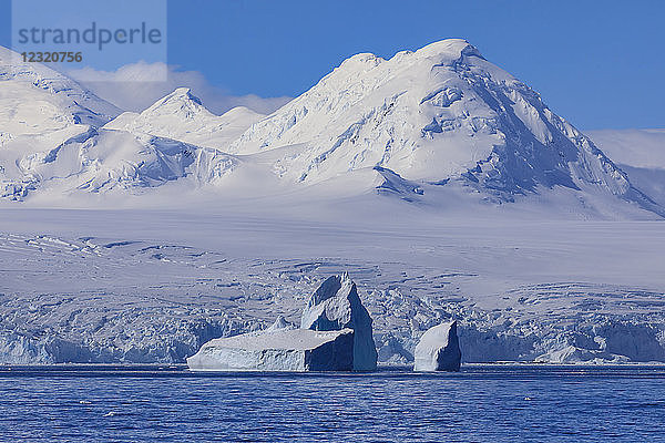 Nicht-tafelförmiger Eisberg vor der vergletscherten  gebirgigen Anvers-Insel  blauer Himmel  Antarktische Halbinsel  Antarktis  Polarregionen