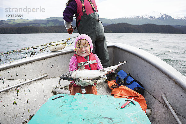 Junges Mädchen hält einen frisch gefangenen Lachs in der Hand  während sie mit ihrer Mutter im Netzskiff ihrer Familie unterwegs ist  Seldovia  Süd-Zentral-Alaska; Alaska  Vereinigte Staaten von Amerika
