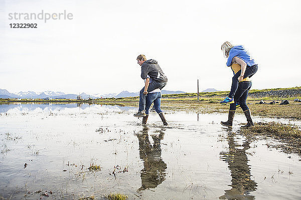 Freunde in Gummistiefeln  die Freunde durch eine nasse Küstengegend tragen  Süd-Zentral-Alaska; Homer  Alaska  Vereinigte Staaten von Amerika