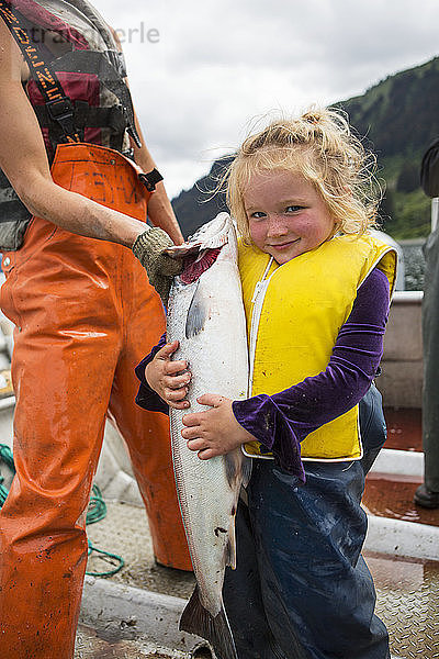 Junges Mädchen  das einen großen Rotlachs hält  während es in einem Skiff mit Stellnetz steht  Süd-Zentral-Alaska; Seldovia  Alaska  Vereinigte Staaten von Amerika