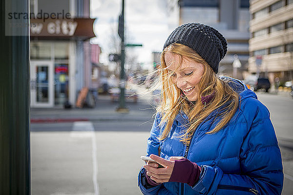 Junge Frau schreibt eine SMS auf ihrem Smartphone in der Innenstadt von Anchorage  Süd-Zentral-Alaska; Anchorage  Alaska  Vereinigte Staaten von Amerika