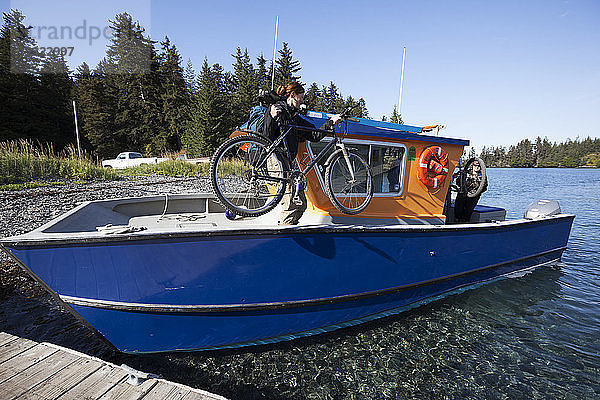 Frau lädt ihr Fahrrad auf ein Wassertaxi  Kenai-Halbinsel  Süd-Zentral-Alaska; Alaska  Vereinigte Staaten von Amerika