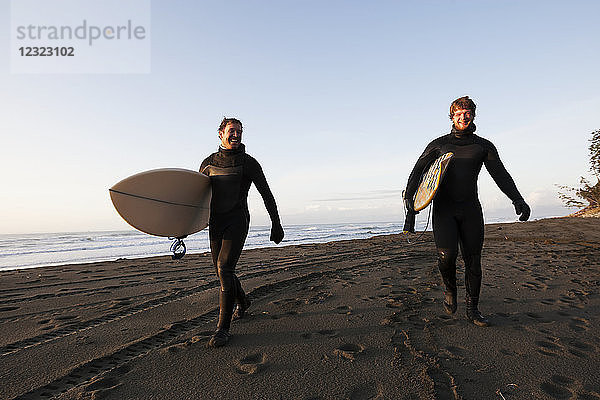 Zwei Surfer  die mit ihren Brettern an einem Strand spazieren gehen  Südost-Alaska; Yakutat  Alaska  Vereinigte Staaten von Amerika