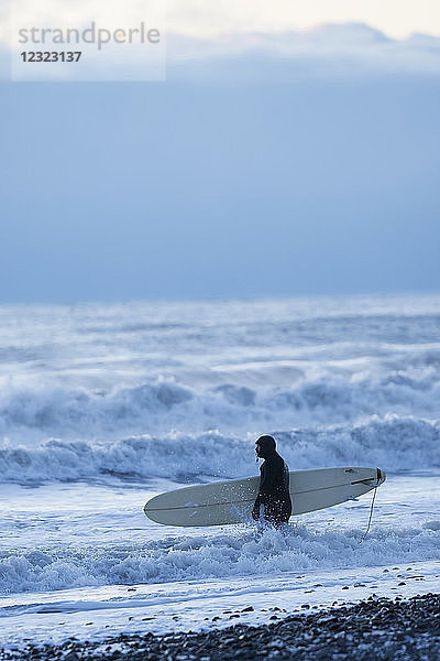 Surfer mit Surfbrett im plätschernden Wasser entlang des Ufers  Kachemak Bay  Süd-Zentral-Alaska; Homer  Alaska  Vereinigte Staaten von Amerika