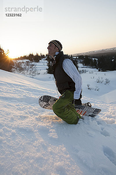 Mann  der bei Sonnenuntergang mit einem Snowboard bergauf geht  in der Nähe von Homer  Süd-Zentral-Alaska; Alaska  Vereinigte Staaten von Amerika
