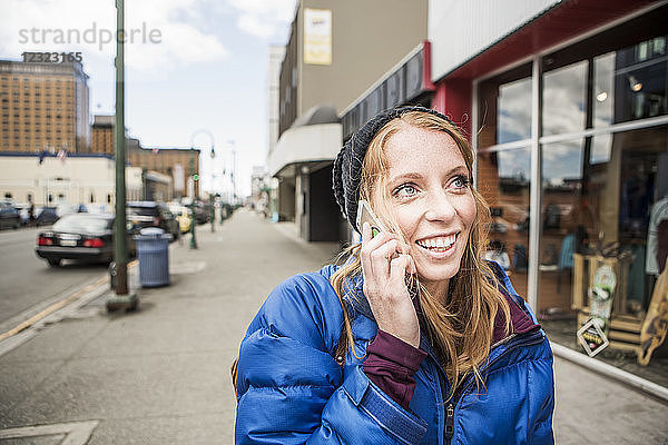 Junge Frau spricht mit ihrem Smartphone in der Innenstadt von Anchorage  Süd-Zentral-Alaska; Anchorage  Alaska  Vereinigte Staaten von Amerika