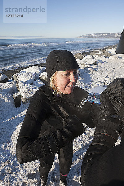 Weibliche Surferin im Neoprenanzug bekommt etwas Wasser zu trinken  Homer Spit Strand im Winter  Süd-Zentral-Alaska; Homer Spit  Alaska  Vereinigte Staaten von Amerika