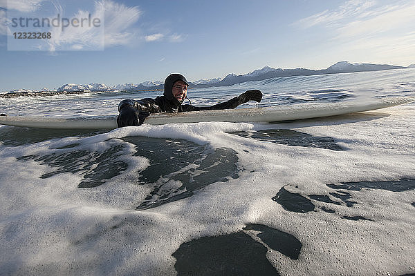 Mann schwimmt mit seinem Surfbrett  Süd-Zentral-Alaska; Homer  Alaska  Vereinigte Staaten von Amerika