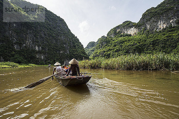 Menschen in einem Boot auf dem Fluss Ngo Dong  umgeben von Kalkstein-Karstbergen; Tam Coc  Ninh Binh  Vietnam