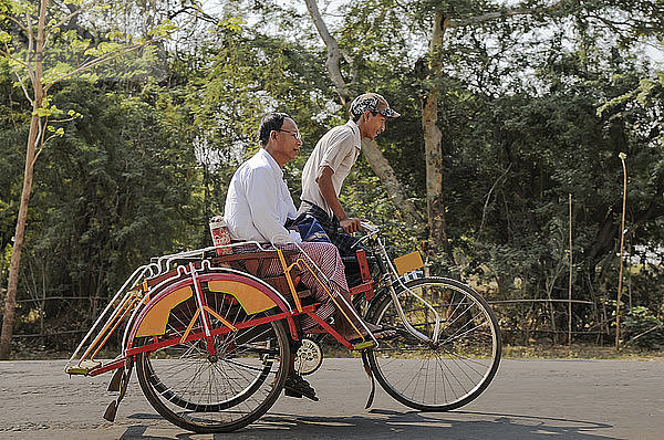Ein junger Mann streichelt einen älteren Mann auf einer Fahrrad-Rikscha; Bagan  Myanmar