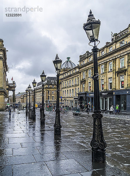 Dekorative Laternenpfähle in einer Reihe entlang einer nassen Straße mit Fußgängern und Geschäften; Newcastle Upon Tyne  Tyne and Wear  England