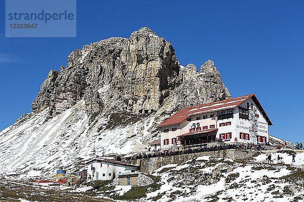 Großes Berghotel auf einem schneebedeckten Bergrücken mit Wanderern  Bergen und blauem Himmel; Sexten  Bozen  Italien