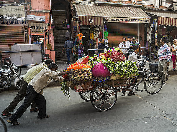 Männer schieben einen Wagen voller frischer Produkte die Straße hinunter; Jaipur  Rajasthan  Indien