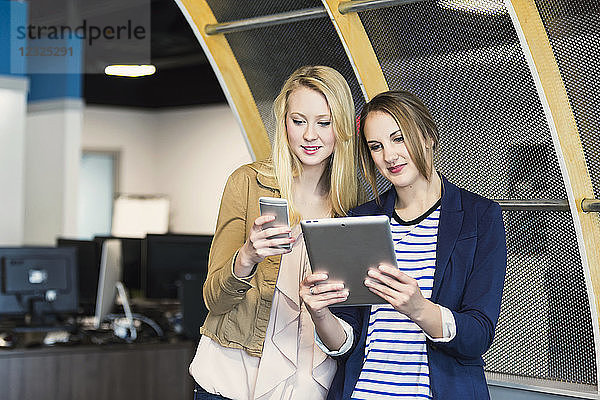 Zwei hübsche junge Geschäftsfrauen der Jahrtausendwende nutzen Technologie am Arbeitsplatz; Sherwood Park  Alberta  Kanada