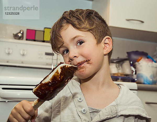Ein grinsender Junge mit unordentlichem Gesicht leckt die Schokolade vom Spatel  nachdem er Karamell gemacht hat; Langley  British Columbia  Kanada