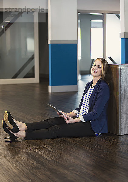 Porträt einer jungen Geschäftsfrau  die auf dem Boden sitzend Technologie am Arbeitsplatz nutzt; Sherwood Park  Alberta  Kanada