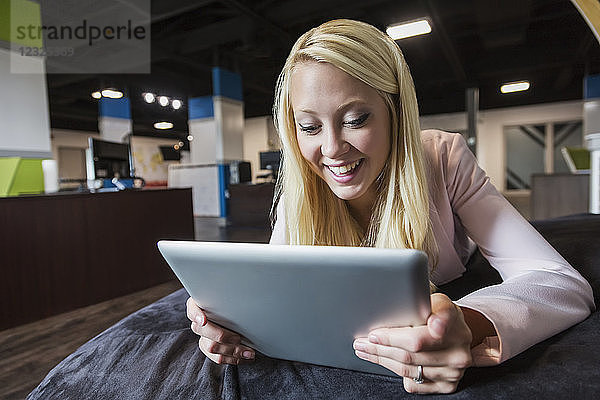 Schöne junge Geschäftsfrau mit langen blonden Haaren am Arbeitsplatz auf einem Sitzsack und einem Tablet; Sherwood Park  Alberta  Kanada