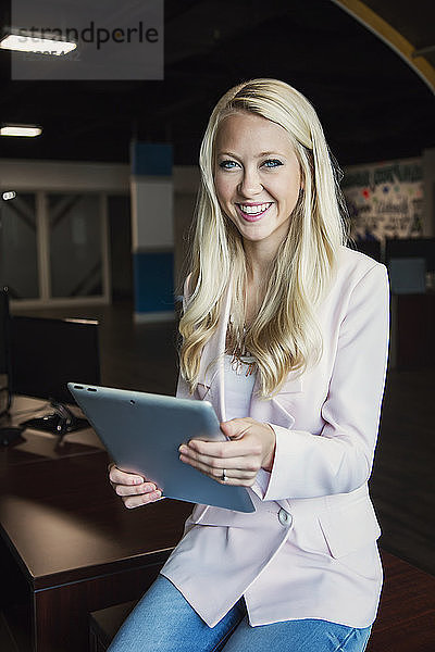 Business-Porträt einer schönen jungen Geschäftsfrau mit langen blonden Haaren  die ein Tablet hält und für die Kamera am Arbeitsplatz posiert; Sherwood Park  Alberta  Kanada