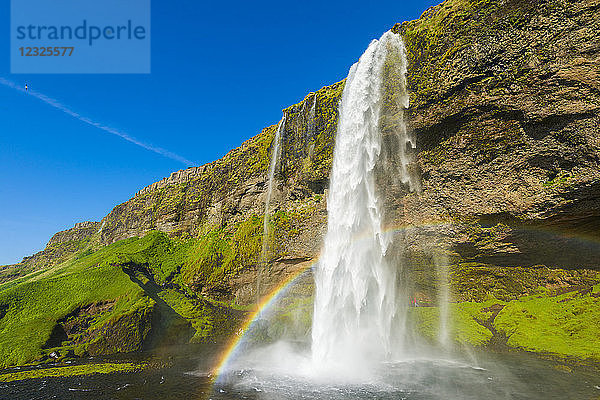 Skogafoss-Wasserfall mit blauem Himmel und einem Regenbogen im Nebel; Island