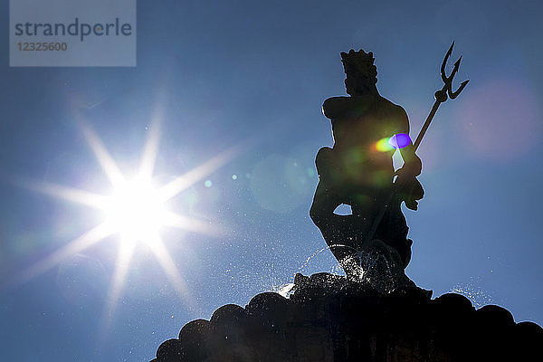 Silhouette einer Statue auf einem Brunnen mit Sonnenaufgang und blauem Himmel; Trento  Trento  Italien