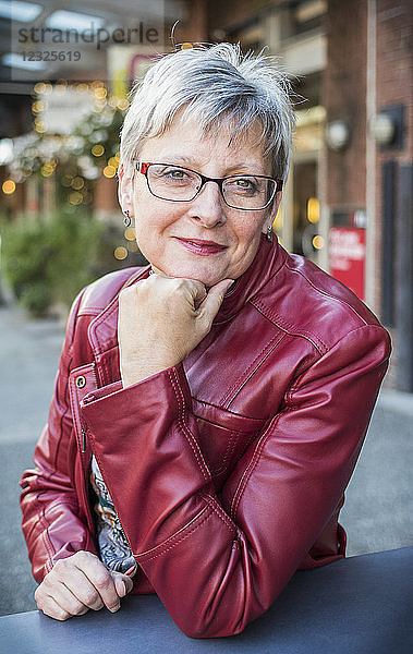 Porträt einer reifen Frau in einer roten Lederjacke  die an einem Tisch sitzt und ihr Kinn in die Hand stützt; Vancouver  British Columbia  Kanada