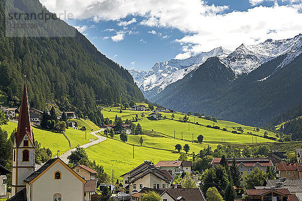 Alpendorf mit Kirchturm  grünen Wiesen im Tal und schneebedeckten Bergen in der Ferne; St. Jodok  Tirol  Österreich