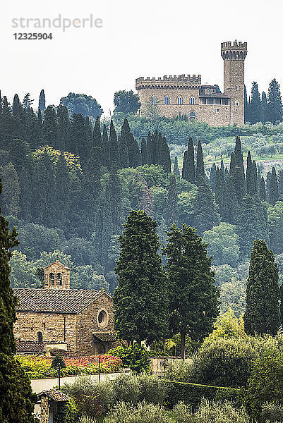 Ein mit Bäumen bewachsener Hügel im Nebel  eine Steinkirche im Tal und ein Schloss auf dem Hügel; Italien