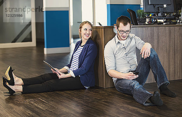 Zwei junge Berufstätige der Jahrtausendwende machen eine Pause und sitzen auf dem Boden ihres Arbeitsplatzes und nutzen die Technologie; Sherwood Park  Alberta  Kanada