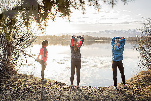 Drei junge Frauen  die sich auf einem Pfad am Ufer des Wassers strecken; Anchorage  Alaska  Vereinigte Staaten von Amerika