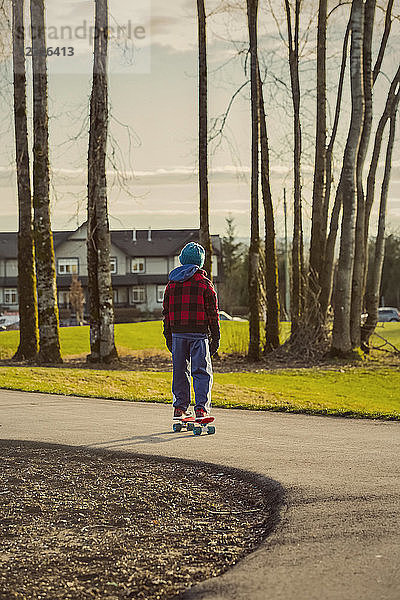 Ein kleiner Junge fährt im Herbst auf einem Skateboard auf einem Weg; Langley  British Columbia  Kanada