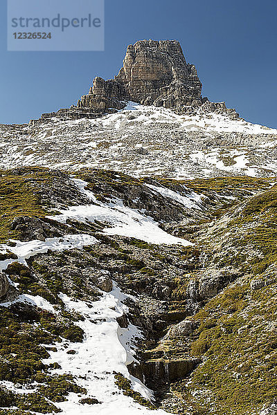 Berggipfel über einem schneebedeckten Hang mit einem kleinen Bach und blauem Himmel; Sexten  Bozen  Italien