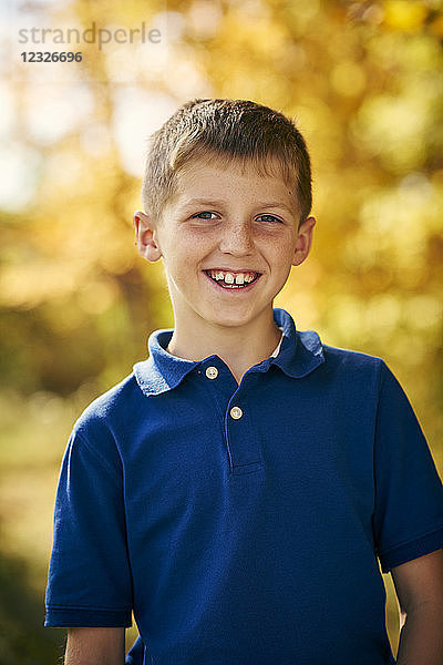 Porträt eines kleinen Jungen mit einem breiten Grinsen und herbstlichem Laub im Hintergrund; Ontario  Kanada