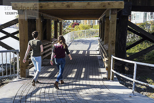 Zwei junge Frauen gehen gemeinsam einen Weg unter einer Brücke in einem Park entlang; New Westminster  British Columbia  Kanada