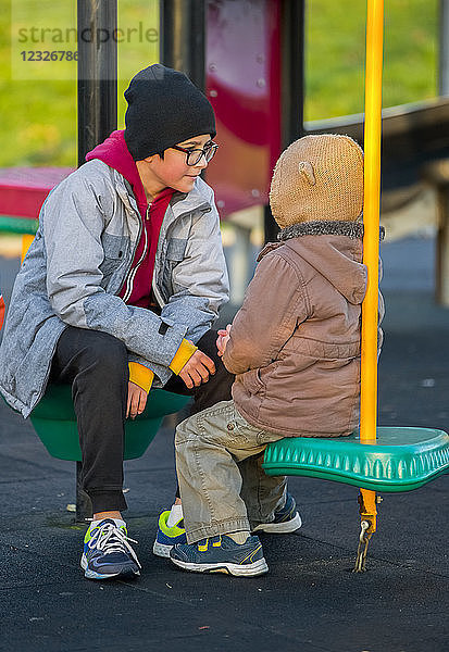 Ein kleiner Junge und sein älterer Bruder sitzen und unterhalten sich auf einem Spielplatz; Langley  British Columbia  Kanada