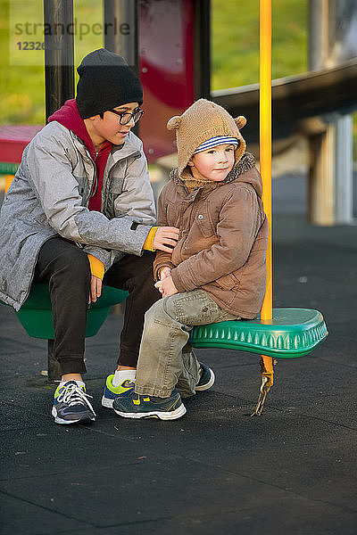 Ein kleiner Junge und sein älterer Bruder sitzen und unterhalten sich auf einem Spielplatz; Langley  British Columbia  Kanada