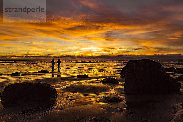 Silhouette von zwei Personen  die am Wreck Beach stehen und bei Sonnenuntergang orange leuchten; Vancouver  British Columbia  Kanada