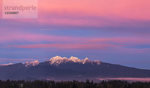 Dramatische leuchtende Wolken über den schneebedeckten Bergen  die sich auf dem Schnee darunter spiegeln; British Columbia  Kanada