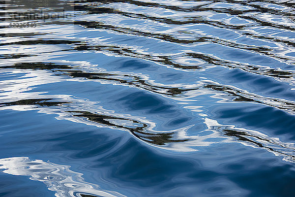 Die blauen  schwarzen und weißen Reflexionen des Himmels  der Wolken und des nahegelegenen Landes im Kielwasser eines Bootes im Puget Sound  Washington  erzeugen eine schöne Textur und ein Gefühl der Bewegung; Puget Sound  Washington  Vereinigte Staaten von Amerika