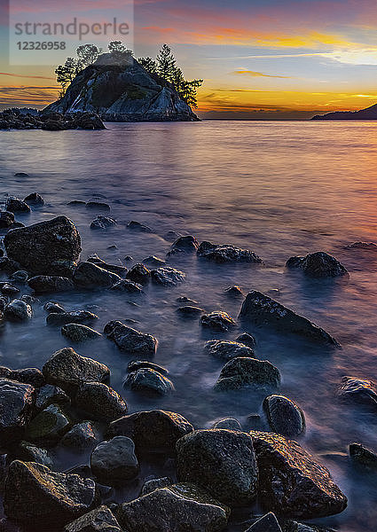 Goldenes Sonnenlicht beleuchtet die Wolken in der Ferne und nasse Felsen entlang der Küste; Vancouver  British Columbia  Kanada