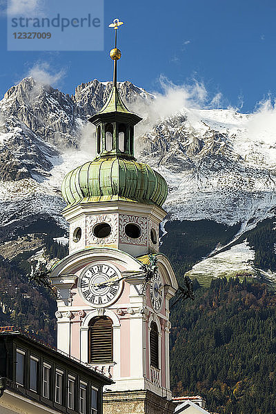 Dekorativer Kirchturm mit Wald und schroffen  schneebedeckten Gipfeln und blauem Himmel im Hintergrund; Innsbruck  Tirol  Österreich