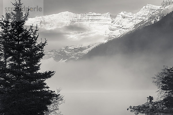 Silhouette eines Fotografen am Ufer des Lake Louise mit vom See aufsteigendem Nebel bei Sonnenaufgang  Banff National Park; Lake Louise  Alberta  Kanada