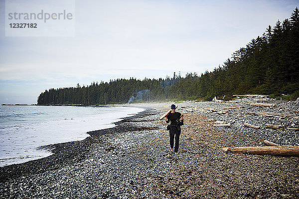 Eine Frau geht an einem felsigen Strand entlang und sammelt Brennholz im Cape Scott Provincial Park  Vancouver Island; British Columbia  Kanada