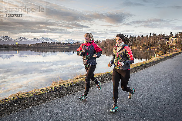 Zwei junge Frauen laufen auf einem Pfad am Wasser mit Bergen in der Ferne; Anchorage  Alaska  Vereinigte Staaten von Amerika