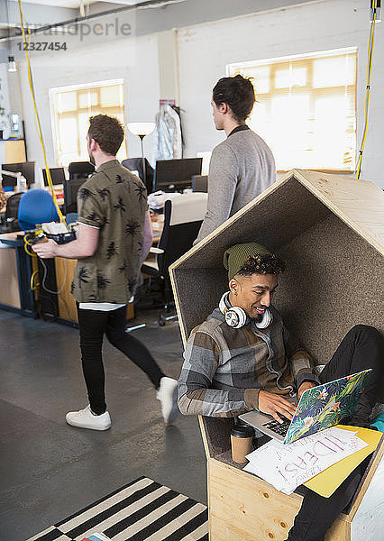 Creative businessman with headphones using laptop in office cubby