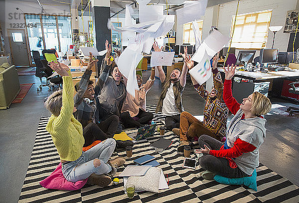 Playful  enthusiastic creative business team throwing paperwork overhead in open plan office